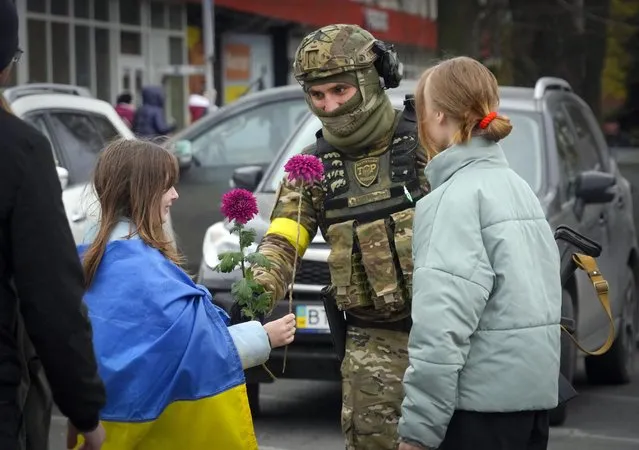 A girl wrapped in the national flag exchange flowers with a Ukrainian soldier in central Kherson, Ukraine, Sunday, November 13, 2022. The Russian retreat from Kherson marked a triumphant milestone in Ukraine's pushback against Moscow's invasion almost nine months ago. (Photo by Efrem Lukatsky/AP Photo)