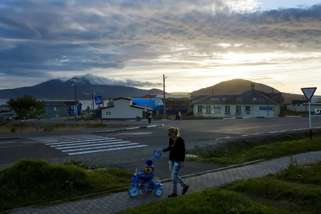 A woman pushes a child on a tricycle at sunset in the centre of Yuzhno-Kurilsk, the main settlement on the Southern Kurile island of Kunashir September 15, 2015. (Photo by Thomas Peter/Reuters)