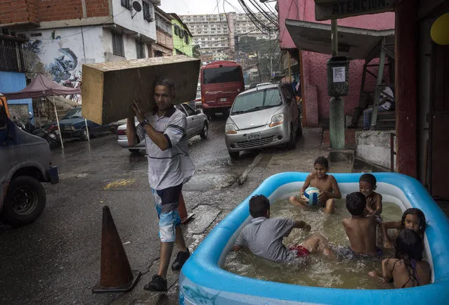 Children play in an inflatable swimming pool in the working class 23 de Enero neighborhood as it rains lightly in Caracas, Venezuela, Saturday, October 21, 2017. (Photo by Rodrigo Abd/AP Photo)