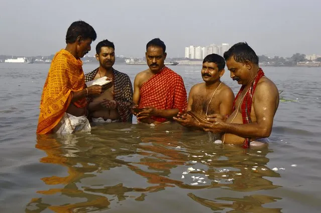 A Hindu priest (L) performs Tarpana, a religious ritual, as he helps the men to pray on the banks of the Ganges river on the holy day of Mahalaya in Kolkata, India, October 12, 2015. Hindus offer prayers with holy water after taking a dip in the river to honour the souls of their departed ancestors during Mahalaya, which is also called Pitru Paksha. (Photo by Rupak De Chowdhuri/Reuters)