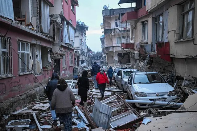 People walk along a street strewn with debris as they look for relatives in Hatay, the day after a 7.8-magnitude earthquake struck the country's southeast on February 7, 2023. Rescuers in Turkey and Syria braved frigid weather, aftershocks and collapsing buildings, as they dug for survivors buried by an earthquake that killed more than 5,000 people. Up to 23 million people could be affected by the massive earthquake that has killed thousands in Turkey and Syria, the WHO warned on Tuesday, promising long-term assistance. (Photo by Bulent Kilic/AFP Photo)