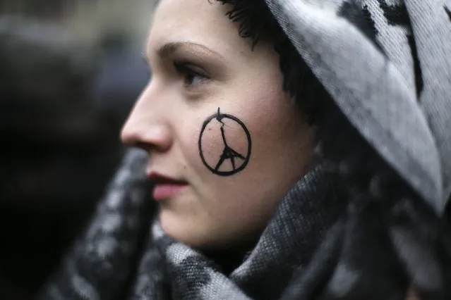 A woman has a peace sign combined with the Eiffel Tower painted on her face as she arrives for a minute of silence  for the  victims of Friday's attacks in Paris, in front of the French Embassy in Berlin, Sunday, November 15, 2015.  Multiple attacks across Paris on Friday night have left scores dead and hundreds injured. (Photo by Markus Schreiber/AP Photo)