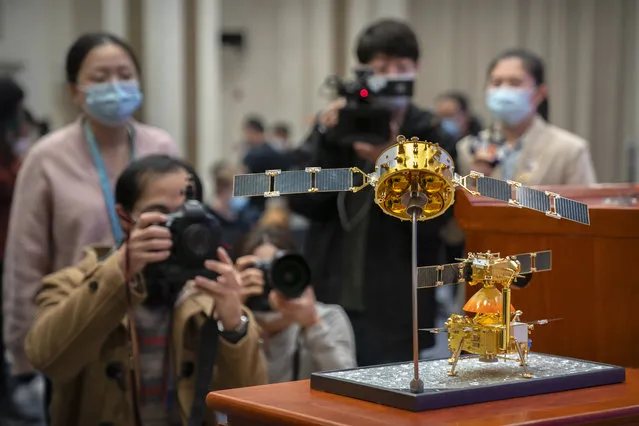 Journalists wearing face masks to prevent the spread of the coronavirus take photos of a model of China's Chang'e 5 lunar orbiter and lander before a press conference at the State Council Information Office in Beijing, Thursday, December 17, 2020. Following the successful return of moon rocks by its Chang'e 5 robotic probe, China is preparing for future missions that could set the stage for an eventual lunar base to host human explorers. (Photo by Mark Schiefelbein/AP Photo)