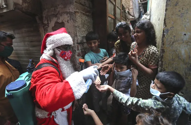 A man dressed as Santa Claus sanitizes hands of children in a narrow lane in Dharavi, one of Asia's biggest slums, in Mumbai, India, Saturday, December 19, 2020. India's coronavirus cases have crossed 10 million with new infections dipping to their lowest levels in three months, as the country prepares for a massive COVID-19 vaccination in the new year. (Photo by Rafiq Maqbool/AP Photo)