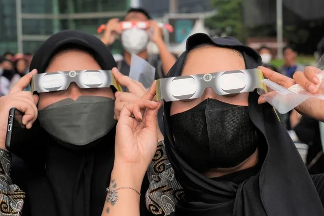 Indonesian women use protective glasses to watch solar eclipse in Jakarta, Indonesia, Thursday, April 20, 2023. The lucky few in the path of the hybrid solar eclipse would either get plunged into the darkness of a total eclipse or see a “ring of fire” as the sun peeks out from behind the moon. (Photo by Tatan Syuflana/AP Photo)