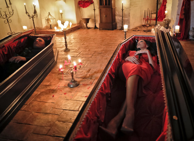 Tami Varma, right, and her brother Robin, the grandchildren of Devendra Varma, a scholar of English gothic tales and an expert in vampire lore, pose in coffins at the Bran Castle, in Bran, Romania, Monday, October 31, 2016. A Canadian brother and sister are passing Halloween night curled up in red velvet coffins in the Transylvanian castle that inspired the Dracula legend, the first time in 70 years anyone has spent the night in the gothic fortress, after they bested 88,000 people who entered a competition hosted by Airbnb to get the chance to dine and sleep at the castle in Romania. A portrait of medieval prince Vlad the Impaler is placed on the wall. (Photo by Vadim Ghirda/AP Photo)