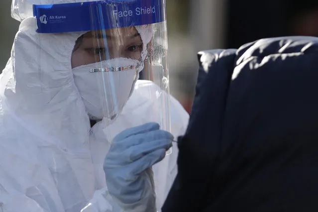 A medical worker wearing protective gear takes samples from a woman during a COVID-19 testing at a coronavirus testing site in Seoul, South Korea on December 12, 2020. South Korea had seemed to be winning the fight against the coronavirus: Quickly ramping up its testing, contact-tracing and quarantine efforts paid off when it weathered an early outbreak without the economic pain of a lockdown. But a deadly resurgence has reached new heights during Christmas week, prompting soul-searching on how the nation sleepwalked into a crisis. (Photo by Lee Jin-man/AP Photo)