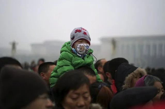 A boy wearing a mask sits on the shoulders of a man as they watch a flag-raising ceremony amid heavy smog at the Tiananmen Square, after the city issued its first ever "red alert" for air pollution, in Beijing, China, December 8, 2015. (Photo by Reuters/Stringer)
