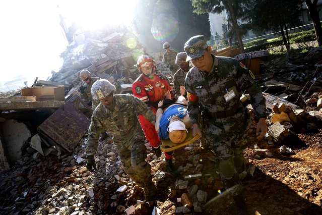 Soldiers from Chinese PLA Southern Theater Command Army and the U.S. Army Pacific carry an injured man from a mocked earthquake-collapsed building as they conducting a joint rescue operation in the U.S.-China Disaster Management Exchange (DME) drill at a PLA's training base in Kunming, southwestern China's Yunnan Province, Friday, November 18, 2016. Hundreds soldiers from China and U.S. conducted the fourth round of Disaster Management Exchange drill on Friday, as part of the exchanges between the two countries' militaries. (Photo by Andy Wong/AP Photo)