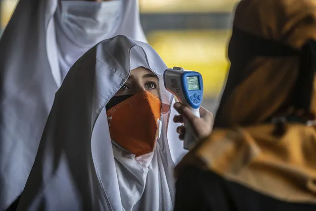 A staff member checks the temperature as students arrive to attend their school in Srinagar, Indian controlled Kashmir, Monday, March 15, 2021. Schools reopened for the lower grades Monday in Indian-controlled Kashmir, eleven months after being closed due to the coronavirus pandemic. (Photo by Mukhtar Khan/AP Photo)