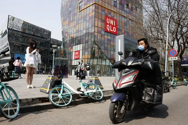A man wearing a mask rides past a Uniqlo store in Beijing on Thursday, March 25, 2021. (Photo by Ng Han Guan/AP Photo)