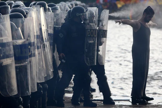 A demonstrator stands in front of riot policemen as they fire pepper spray on his back, during a protest against a constitutional amendment, known as PEC 55, that limits public spending, in front of Brazil's National Congress in Brasilia, Brazil November 29, 2016. (Photo by Adriano Machado/Reuters)