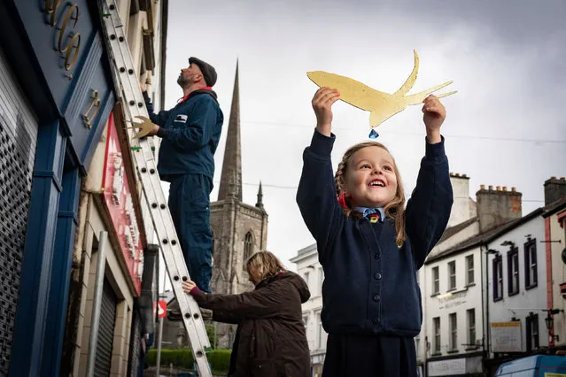 Thea Johnston of Enniskillen integrated primary school helps the artists Simon Carman and Helen Sharp as they begin the installation of 150 swallows in gold leaf in the Northern Irish town, to mark the launch of a new literary tourism initiative on May 11, 2021. (Photo by Brian Morrison/PA Wire Press Association)