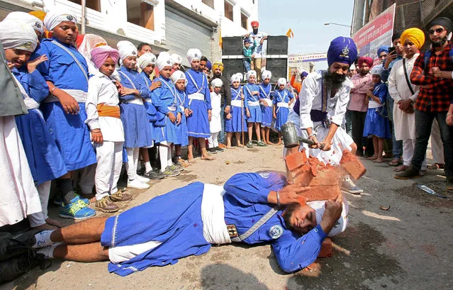 A Nihang or Sikh warrior uses a hammer to break bricks on the head of another Sikh as they perform Gatkha, a traditional form of martial arts, during a religious procession to mark the birth anniversary of Sri Guru Ram Das, the fourth Guru of the Sikhs, in Amritsar, India, October 25, 2018. (Photo by Munish Sharma/Reuters)