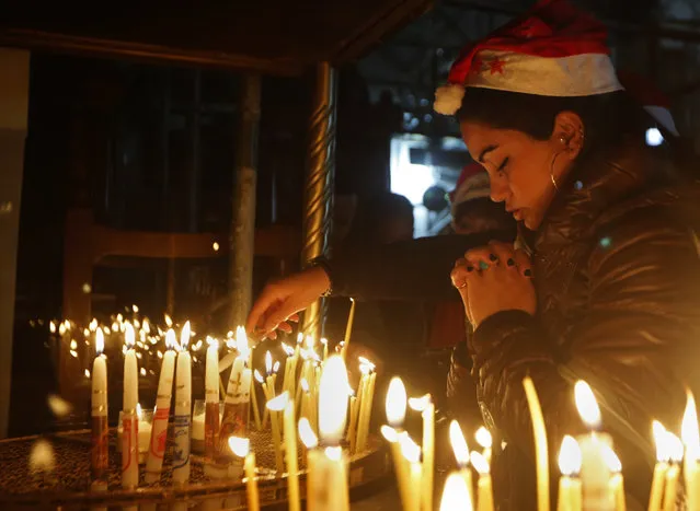 A Christian worshipper prays after lighting a candle on Christmas Eve at the Church of the Nativity, built atop the site where Christians believe Jesus Christ was born, in the West Bank City of Bethlehem, Saturday, December 24, 2016. (Photo by Majdi Mohammed/AP Photo)