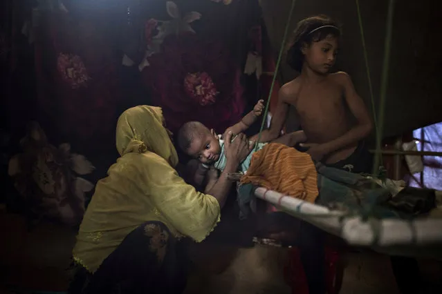 M's daughter, right, hands over her baby brother to their mother in their shelter in Kutupalong refugee camp in Bangladesh on Tuesday, June 26, 2018. M was raped by six soldiers from Myanmar's security forces after they strangled her 2-year-old son to death. The Hague-based International Criminal Court chief prosecutor Fatou Bensouda says she is launching a preliminary investigation to establish if there is enough evidence to merit a full investigation into deportations of hundreds of thousands of Rohingya Muslims from Myanmar into Bangladesh. (Photo by Wong Maye-E/AP Photo)
