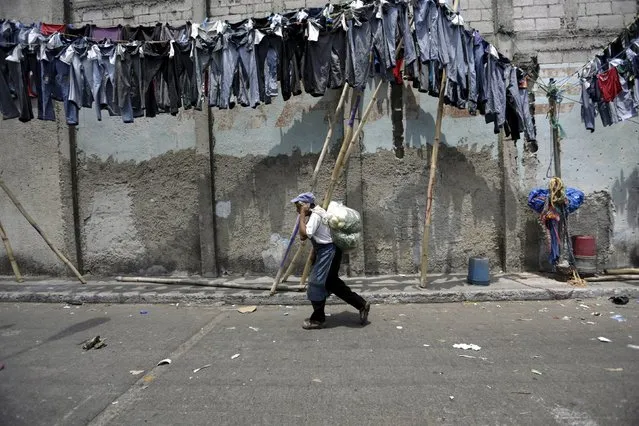 A man carries bags of vegetables while walking next on pants that are hung to dry in the sun on the streets of Guatemala City, April 9, 2015. (Photo by Jorge Dan Lopez/Reuters)