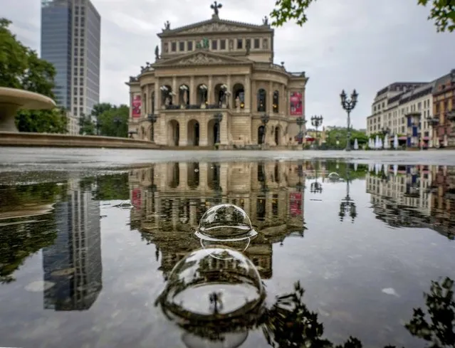 Bubbles caused by rain drops swim on a puddle where the Old Opera is reflected in Frankfurt, Germany, early Tuesday, July 13, 2021. (Photo by Michael Probst/AP Photo)