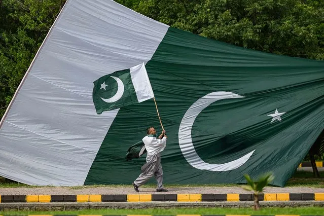 A man holds a national flag of Pakistan as he walks along a street in Islamabad on August 10, 2021, ahead of the country's 75th Independence Day, which marks the end of British colonial rule. (Photo by Aamir Qureshi/AFP Photo)