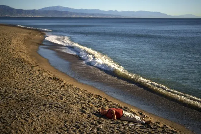 A man rests on the sand of the beach in front of Mediterranean sea in Torremolinos, southern Spain, Wednesday, November 22, 2023. (Photo by Manu Fernandez/AP Photo)