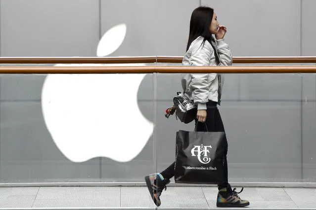 A woman carries a paper bag containing goods purchased from American brand Abercrombie & Fitch walks past an Apple store at the capital city's popular shopping mall in Beijing, Tuesday, February 26, 2019. American companies in China increasingly worry U.S.-Chinese relations will deteriorate and are “hedging their bets” by delaying investment or moving operations, a business group reported Tuesday. (Photo by Andy Wong/AP Photo)
