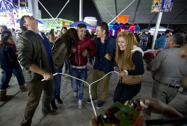 In this April 11, 2015 photo, friends hold hands as they get an electric shock from a vendor at the Texcoco Fair on the outskirts of Mexico City. The machine, called “toques”, or “blasts”, emits varying degrees of electric shocks to paying customers. (Photo by Eduardo Verdugo/AP Photo)