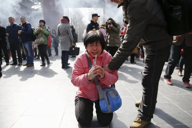 A crying woman falls on her knees as relatives of passengers onboard of Malaysia Airlines flight MH370 which went missing in 2014, burn incense sticks and pray at Lama Temple in Beijing, China, March 8, 2016. (Photo by Damir Sagolj/Reuters)