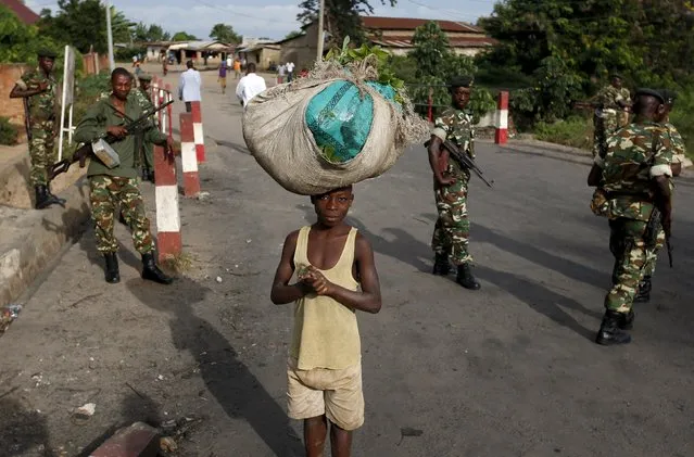 A boy carries goods on top of his head near soldiers during a protest against Burundi President Pierre Nkurunziza and his bid for a third term in Bujumbura, Burundi, May 18, 2015. Small groups of protesters shouted slogans against Burundi President Pierre Nkurunziza and his bid for a third term in office on Monday, resuming street demonstrations days after he survived an attempted coup. (Photo by Goran Tomasevic/Reuters)