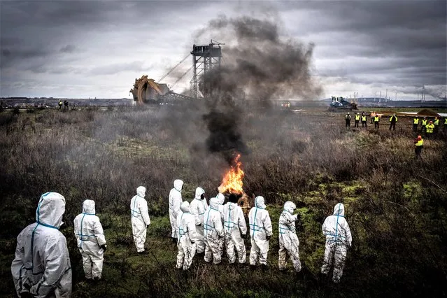 Activists clad in white overalls watch a fire burn in front of a bucket-wheel excavator on January 2, 2023 in Luetzerath, Germany. The village is located on the edge of the still expanding Garzweiler II lignite surface. Despite heavy protests, it will soon be demolished to extract the underlying coal. Protected by riot police, RWE, the mines owning company, started preparations for the eviction of squatters and activists. (photo by Bernd Lauter/Getty Images)