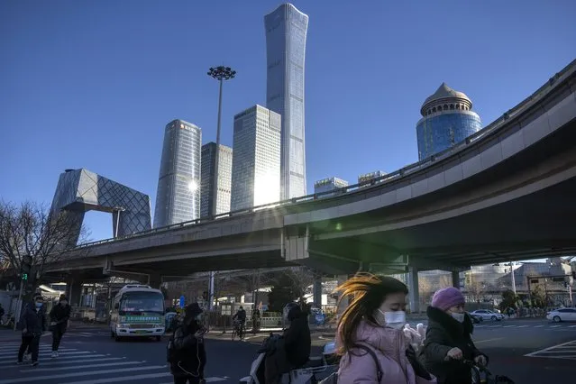 Commuters wearing face masks to help protect against the coronavirus walk across an intersection in the central business district in Beijing, Thursday, January 13, 2022. Just weeks before hosting the Beijing Winter Olympics, China is battling multiple coronavirus outbreaks in half a dozen cities, with the one closest to the capital driven by the highly transmissible omicron variant. (Photo by Mark Schiefelbein/AP Photo)