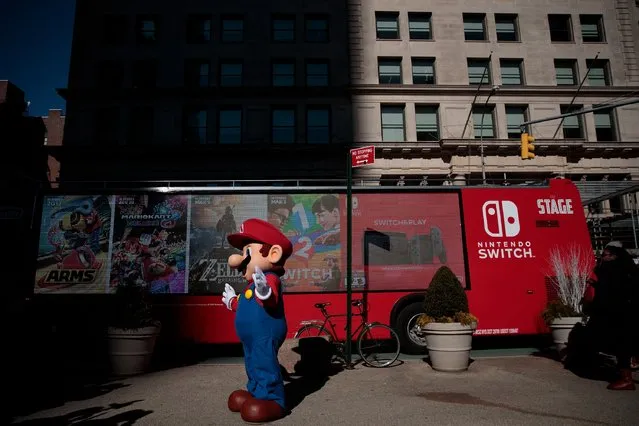 A Nintendo branded bus passes by as a person dressed as the Nintendo character Mario waves at a pop-up Nintendo venue in Madison Square Park, March 3, 2017 in New York City. The Nintendo Switch console goes on sale today and retails for 300 dollars. (Photo by Drew Angerer/Getty Images)