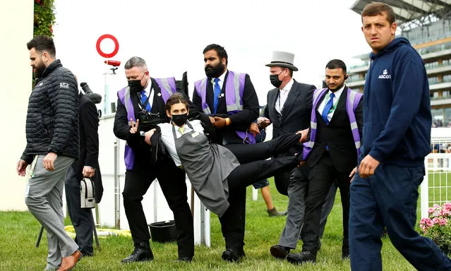 An Extinction Rebellion protester is escorted from the racecourse in Royal Ascot, England on June 19, 2021. Four activists posed as catering staff before unfurling a banner reading “Racing to Extinction”. (Photo by Peter Cziborra/Action Images via Reuters)