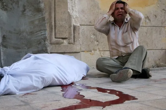 A man reacts next to a body wrapped in shrouds following a reported bombardment with explosive-packed “barrel bombs” by Syrian government forces in the Al-Mowasalat neighborhood in the northern Syrian city of Aleppo on April 27, 2014. Aleppo is divided between government and opposition control, and clashes on the ground, rebel fire and regime aerial bombardment have all increased there in recent weeks. (Photo by Fadi Al-Halabi/AFP Photo)