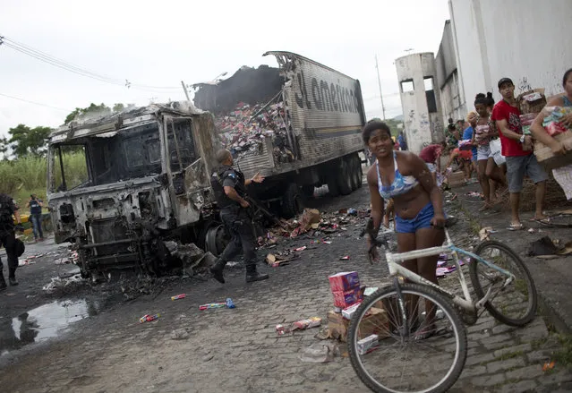 Residents walk past with merchandise they took from a cargo truck, left, allegedly set on fire by drug traffickers, in Rio de Janeiro, Brazil, Tuesday, May 2, 2017. (Photo by Silvia Izquierdo/AP Photo)