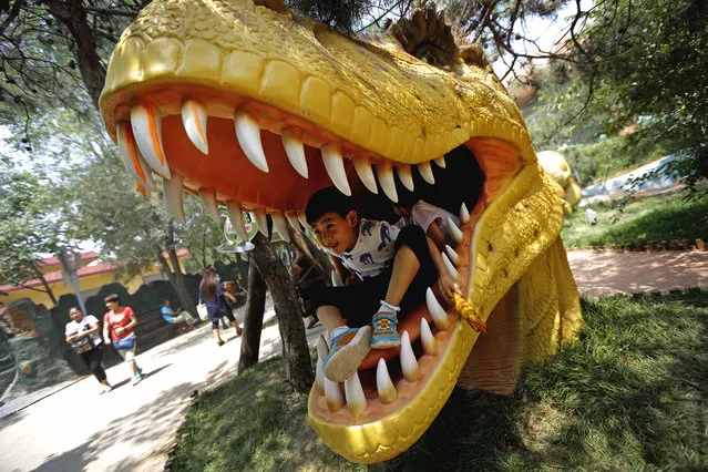 Children play in the mouth of a dinosaur figure at the Shijingshan Amusement Park on International Children's Day in Beijing, China, Wednesday, June 1, 2016. (Photo by Andy Wong/AP Photo)
