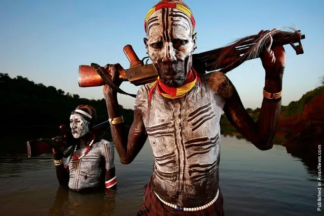 Armed Karo herdsman just back from protecting their cattle herds come down to the river to wash decorative clay markings off their bodies at the end of the day in the Omo Valley, South West Ethiopia. Dus, Omo Valley, Ethiopia, January 2008