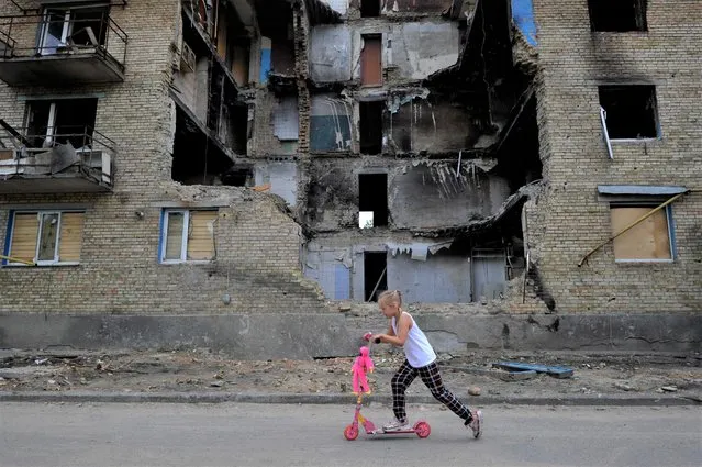 A girl rides a kick scooter past a destroyed residential building in the village of Horenka, Kyiv region, on June 4, 2022 amid the Russian invasion of Ukraine. (Photo by Sergei Chuzavkov/AFP Photo)