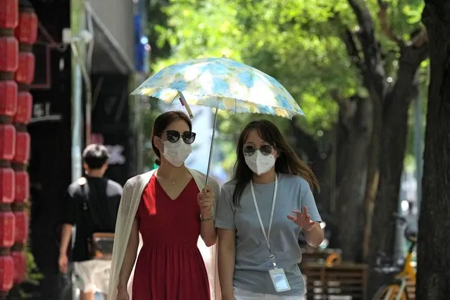 Residents wearing masks walk through a street with trees, Wednesday, July 13, 2022, in Beijing. (Photo by Ng Han Guan/AP Photo)