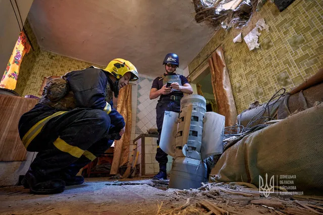 Ukraine's State Emergency Service members inspect an unexploded shell from a Smerch multiple launch rocket system inside a residential apartment, as Russia's attack on Ukraine continues, in Kramatorsk, Ukraine on July 25, 2022. (Photo by Press service of the Donetsk Regional Military Administration/Handout via Reuters)