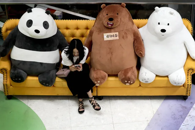 A Chinese woman browses a smartphone on a sofa displaying a panda and bears at a shopping mall in Beijing, Monday, August 21, 2017. Some shopping malls and retailers in the capital city are organizing activities and decorations to attract shoppers as a chance to boost sales in the summer holidays. (Photo by Andy Wong/AP Photo)
