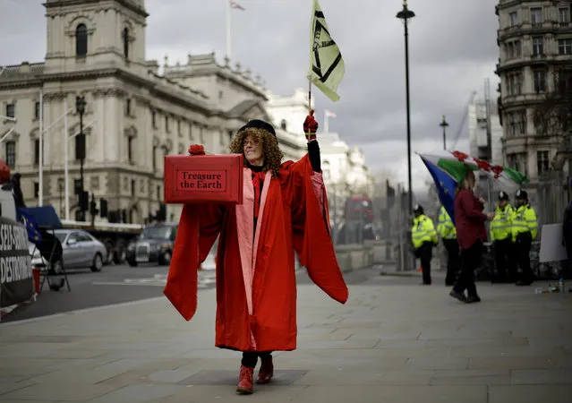 A woman dressed as the Speaker of the House of Commons holds holds a case with a message “treasure the earth” as she participates in a demonstration on the budget outside Parliament in London, Wednesday, March 11, 2020. Britain's Chancellor of the Exchequer Rishi Sunak will announce the first budget since Britain left the European Union. (Photo by Matt Dunham/AP Photo)
