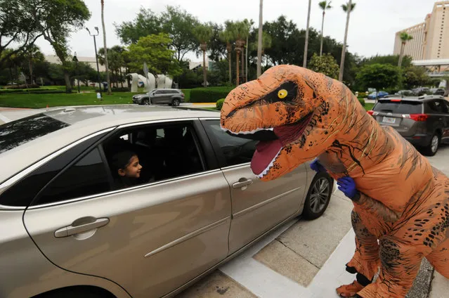 A performer in a dinosaur costume entertains a child in a car parade during the coronavirus outbreak in front of the Orange County Convention Center to celebrate EID, marking the end of the month of Ramadan on May 24, 2020. Families stopped their cars at designated locations where volunteers wearing face masks offered drinks, candy, and toys, and accepted donations for the needy. Over 250 cars participated in the event, which included a car decorating contest. (Photo by Paul Hennessy/SOPA Images/Rex Features/Shutterstock)