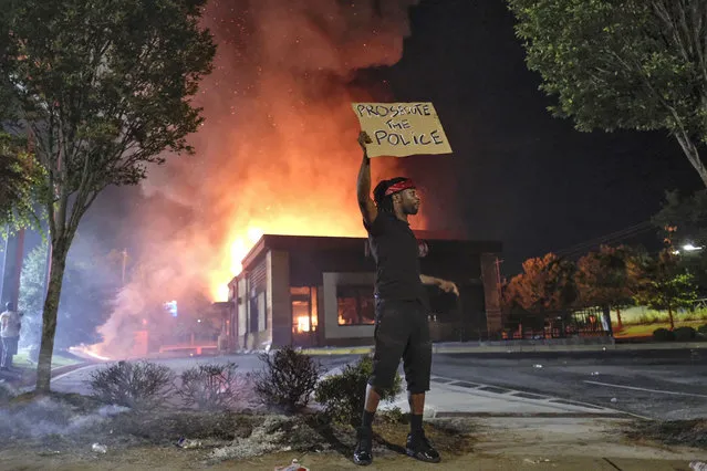A person holds a sign as a Wendy's restaurant burns Saturday, June 13, 2020, in Atlanta after demonstrators set it on fire. Demonstrators were protesting the death of Rayshard Brooks, a black man who was shot and killed by Atlanta police Friday evening following a struggle in the Wendy's drive-thru line. (Photo by Ben GrayAtlanta Journal-Constitution via AP Photo)