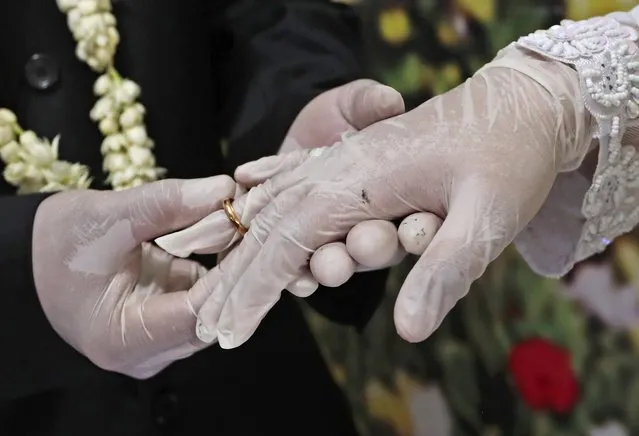 Wearing latex gloves to prevent the spread of the coronavirus, bride Elma Diyani, right, and groom Octavianus Kristianto exchange rings during their wedding ceremony at the local Religious Affairs Office in Pamulang, on the outskirts of Jakarta, Indonesia, Friday, June 19, 2020. (Photo by Tatan Syuflana/AP Photo)