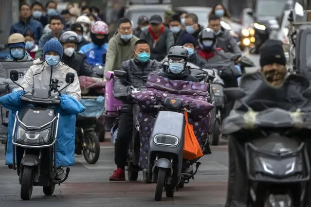 Commuters wearing face masks ride scooters along a street in the central business district in Beijing, Friday, October 28, 2022. (Photo by Mark Schiefelbein/AP Photo)