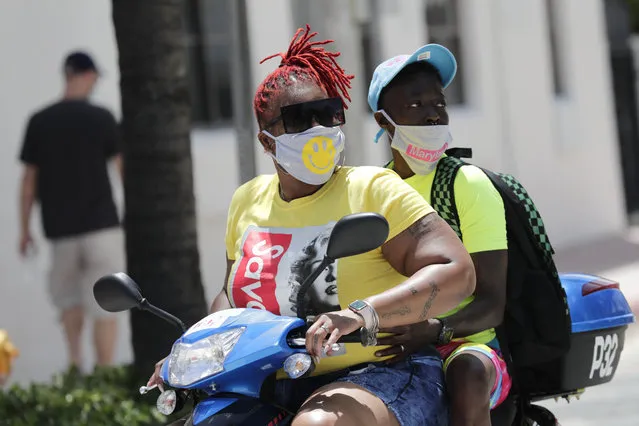 People wearing protective face masks ride a scooter down Ocean Drive during the coronavirus pandemic, Sunday, July 12, 2020, in Miami Beach, Fla. Florida on Sunday reported the largest single-day increase in positive coronavirus cases in any one state since the beginning of the pandemic.(Photo by Lynne Sladky/AP Photo)