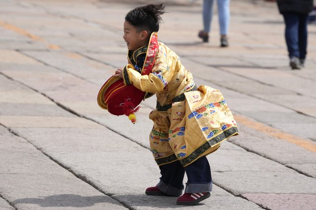 A child dressed as the emperor reacts after retrieving his crown blown away outside the Forbidden City during high winds in Beijing, China, Saturday, April 12, 2025. (Photo by Ng Han Guan/AP Photo)
