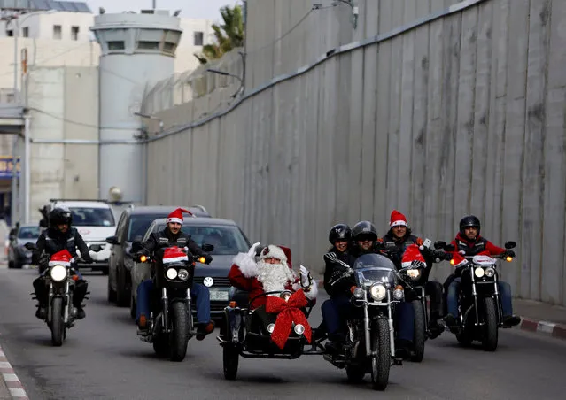 A man dressed as Santa Claus gestures as the convoy of the Latin Patriarch of Jerusalem Pierbattista Pizzaballa arrives through an Israeli checkpoint to attend Christmas celebrations, in the West Bank city of Bethlehem December 24, 2017. (Photo by Mussa Qawasma/Reuters)