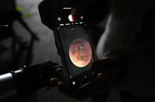 A man uses a smartphone to take picture of a blood moon through telescope during a total lunar eclipse in Goyang, northwest of Seoul, on November 8, 2022. (Photo by Jung Yeon-Je/AFP Photo)