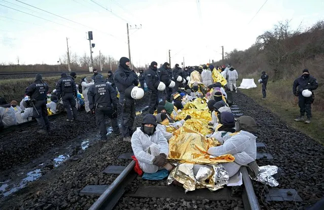 Policemen stand next to environmentalists blocking the railway tracks used to transport lignite to German energy supplier RWE's coal fired power plant in Neurath, western Germany, as demonstrations continue against a coal mine extension in the nearby village of Luetzerath, on January 17, 2023. Already abandoned by its original residents, Luetzerath has become a symbol for resistance against fossil fuels. Energy giant RWE has permission for the expansion of the mine under a compromise agreement that also includes that RWE will stop producing electricity with coal in western Germany by 2030 – eight years earlier than previously planned. With Russia's gas supply cut in the wake of the invasion of Ukraine, Germany has had recourse to coal, firing up mothballed power plants. (Photo by Ina Fassbender/AFP Photo)